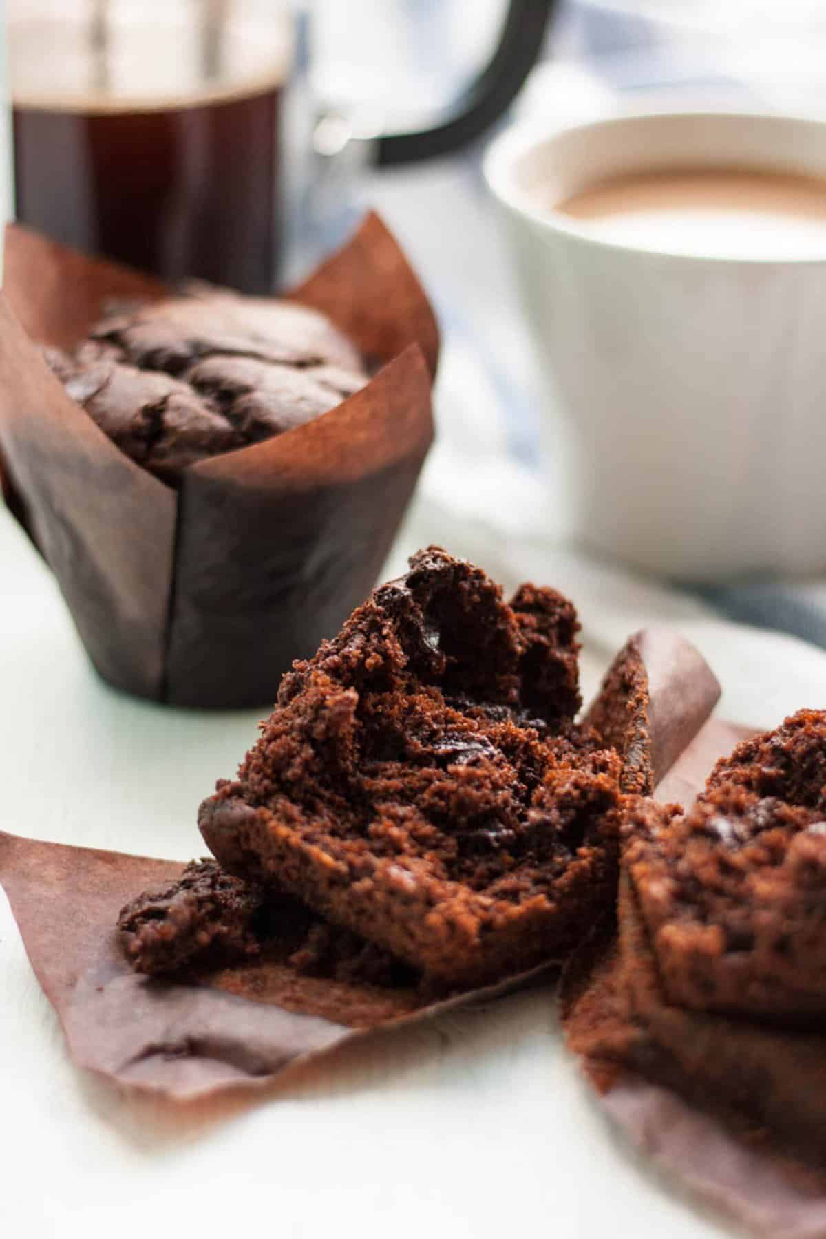Broken open chocolate chip muffin with a mug in the background.