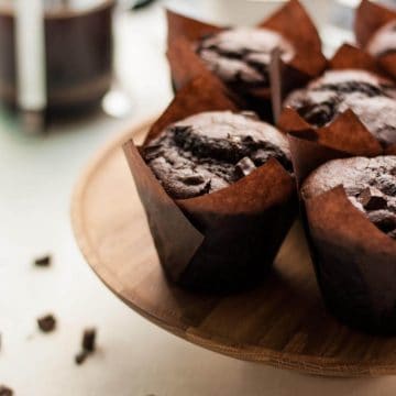 Four chocolate sweet potato muffins on top of a wooden cake stand with a cafetiere.