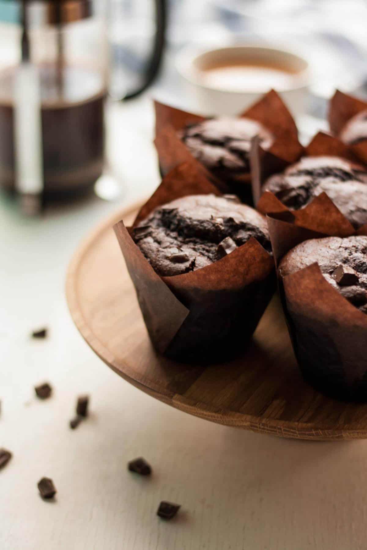 Four chocolate sweet potato muffins on top of a wooden cake stand with a cafetiere.