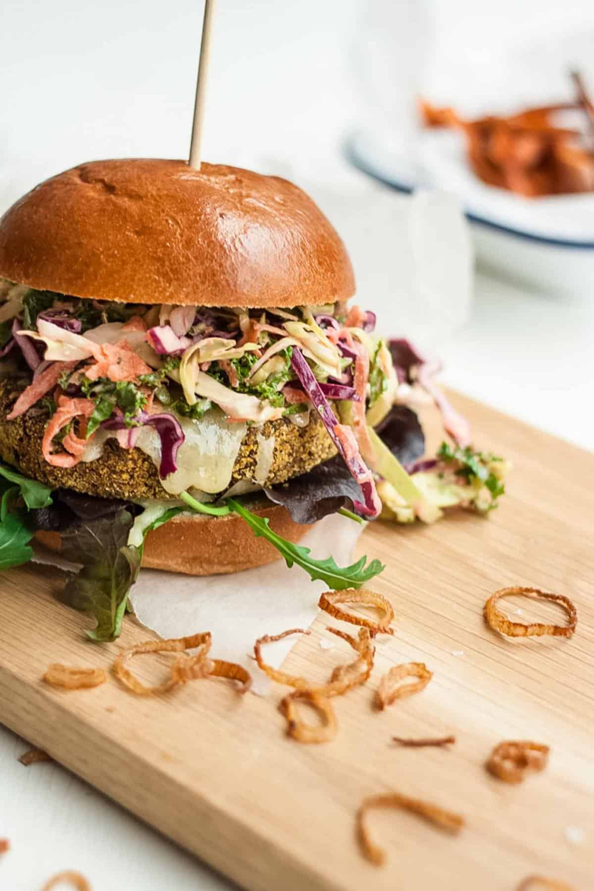 A veggies burger loaded with slaw on a wooden board.