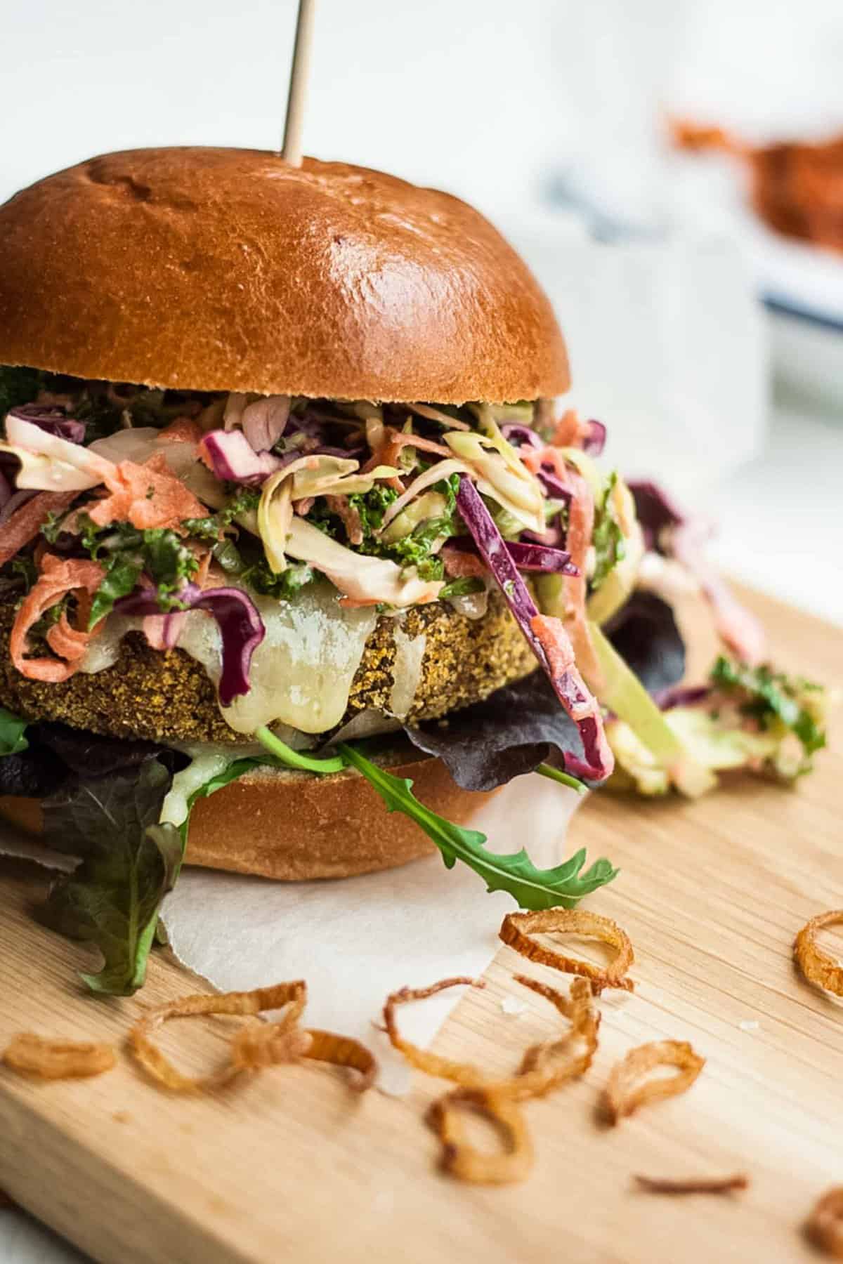 A close up of a veggie burger packed with slaw on a wooden board.