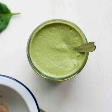 A jar with a green sauce with a spoon.