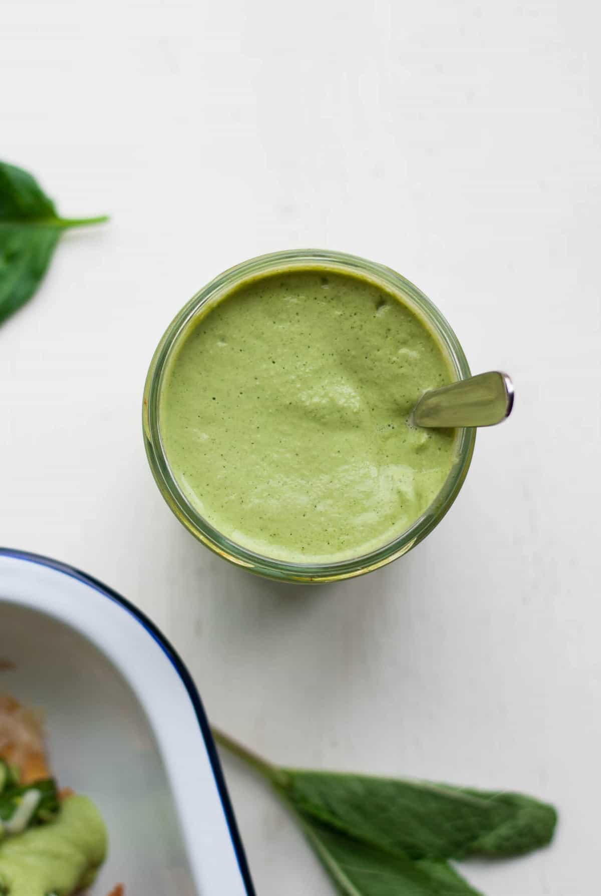 A jar with a green sauce with a spoon. 