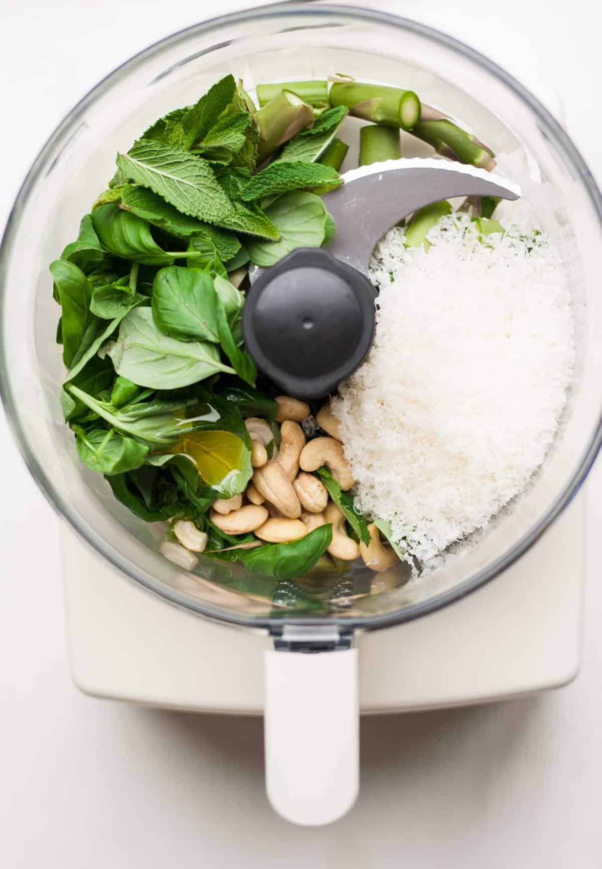 A processor bowl with basil, nuts and cheese.