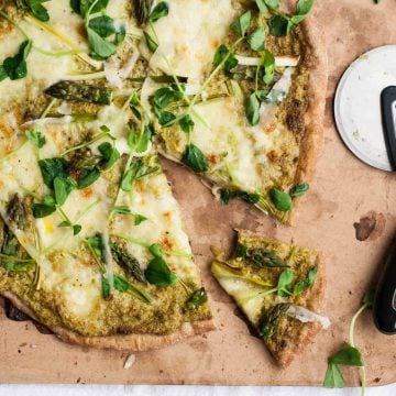 A pizza on a cooking stone with a wedge cut out of it.
