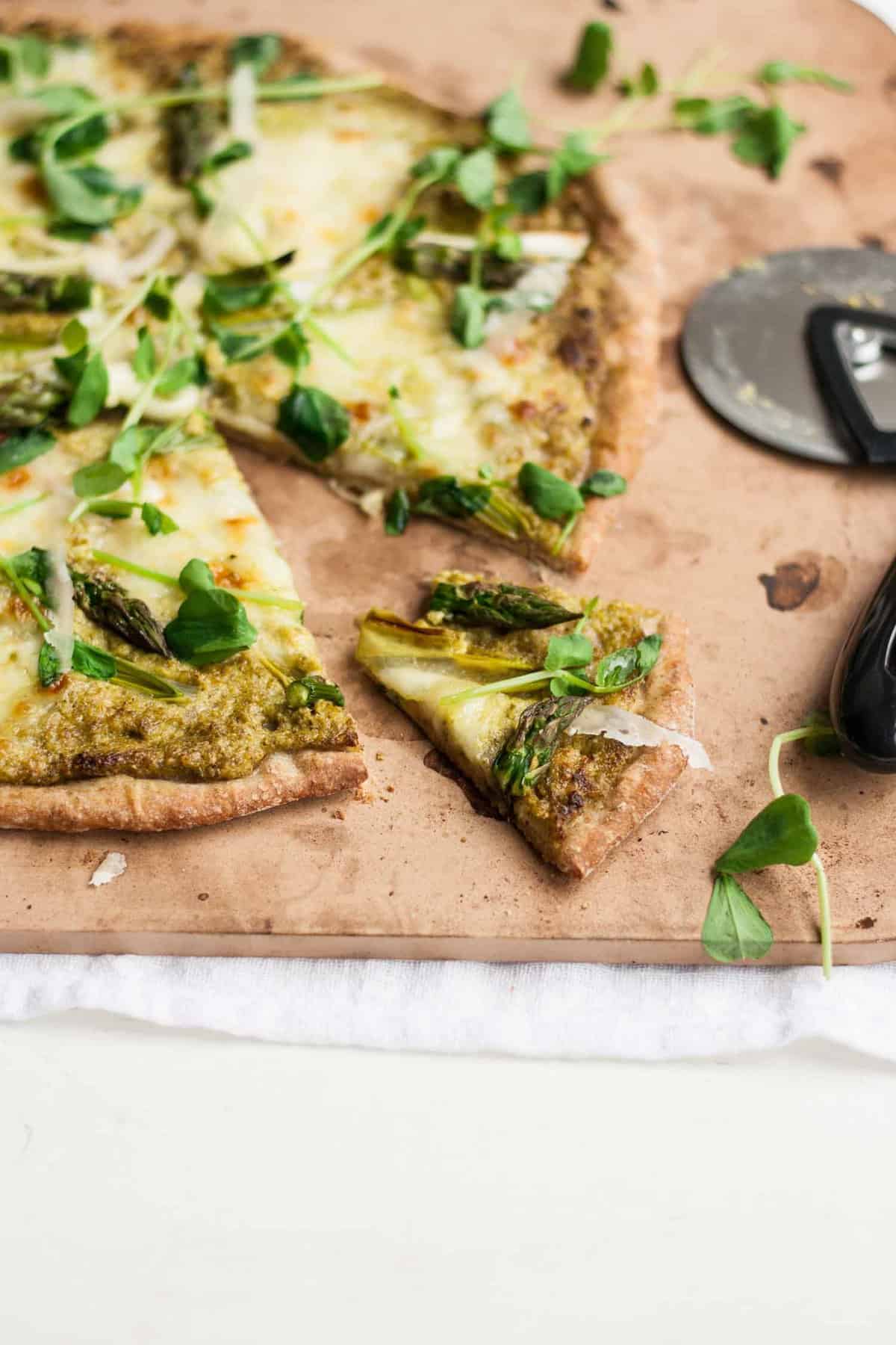 A pizza stone with a wedge cut and pizza cutter to the side.