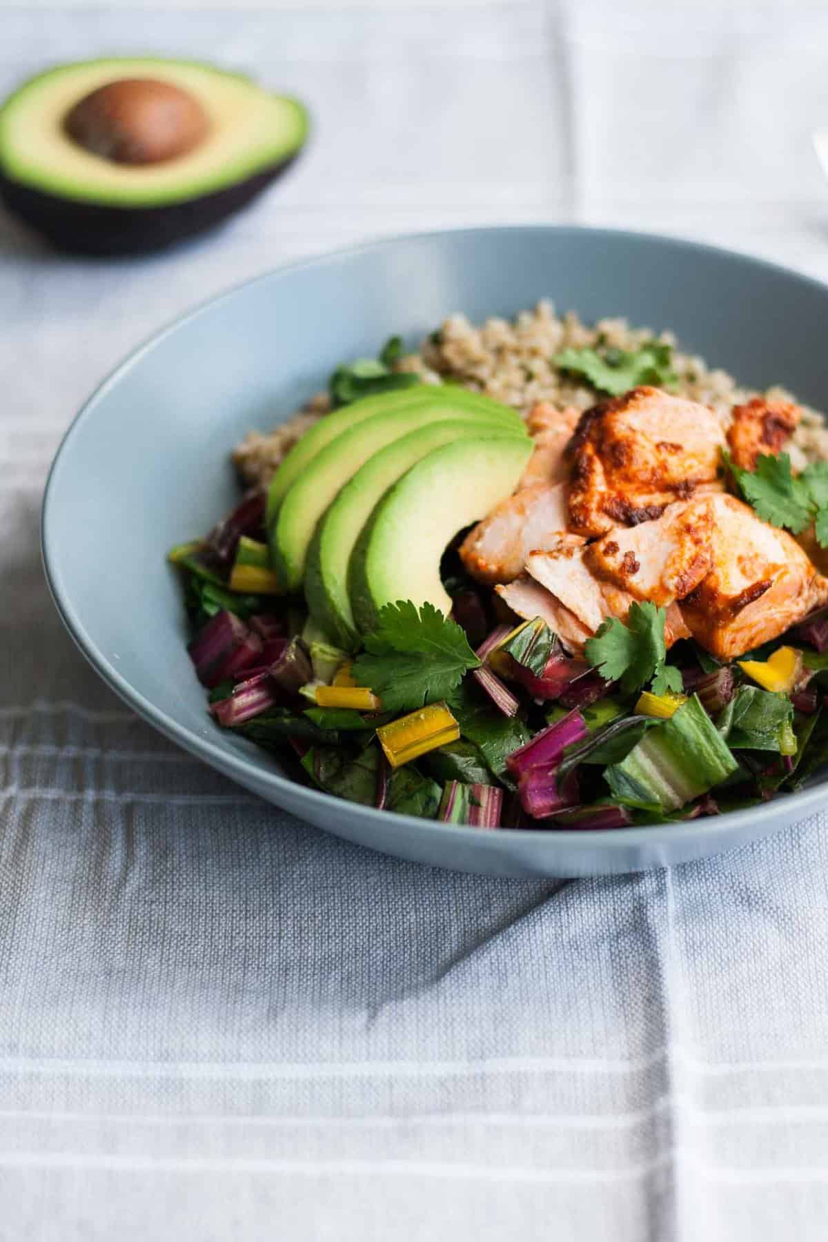 A close up of a bowl showing rainbow coloured chard with salmon and avocado.