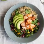 A bowl of grains, salmon and chard with avocado on top.