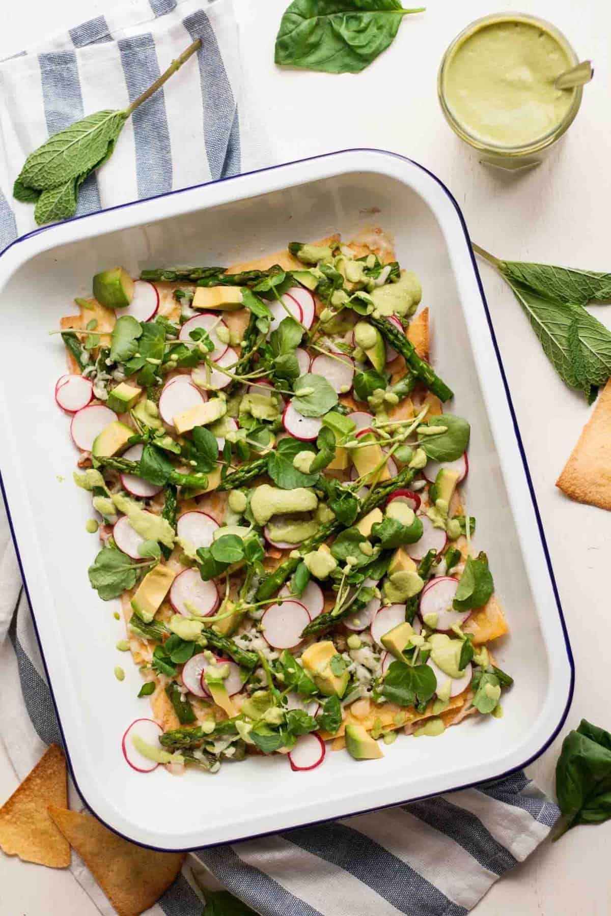 A tray with healthy asparagus nachos topped with avocado and pea shoots.