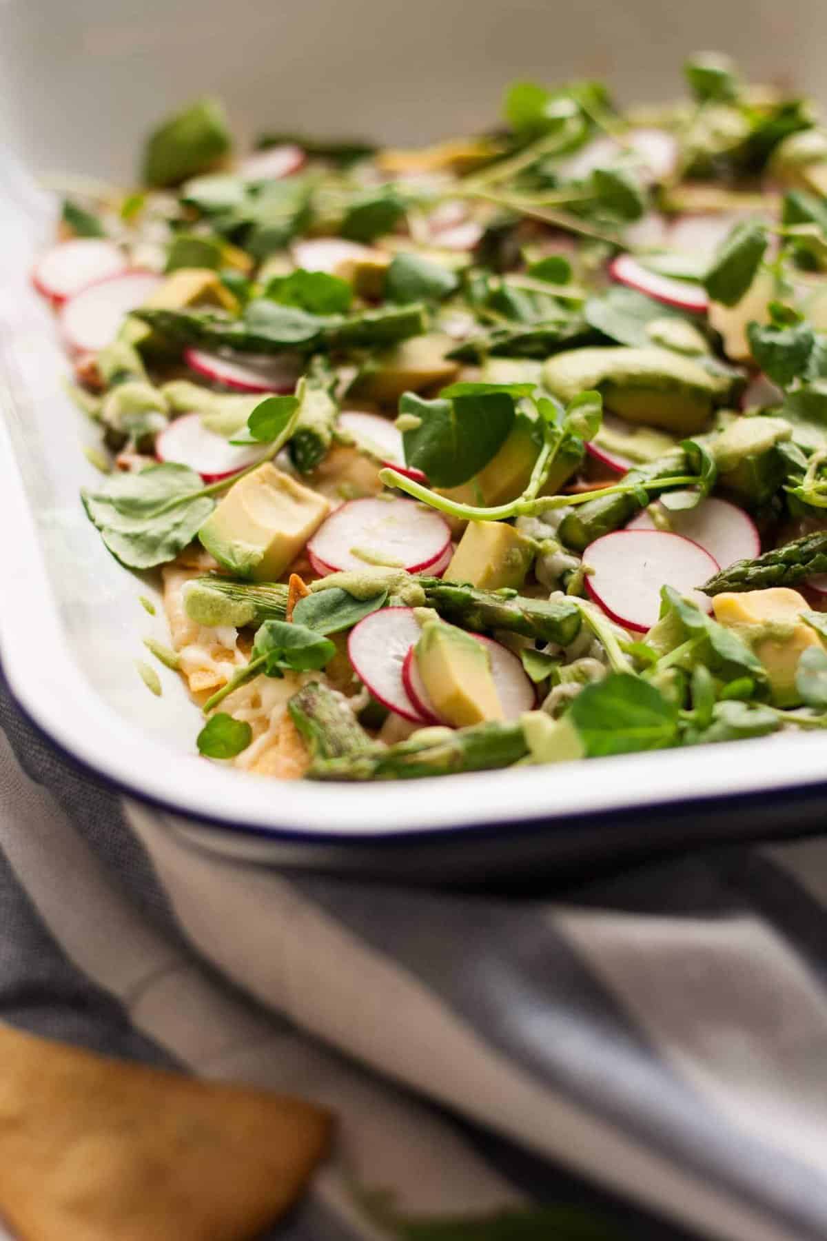 A tray with nachos topped with salad leaves and avocado.