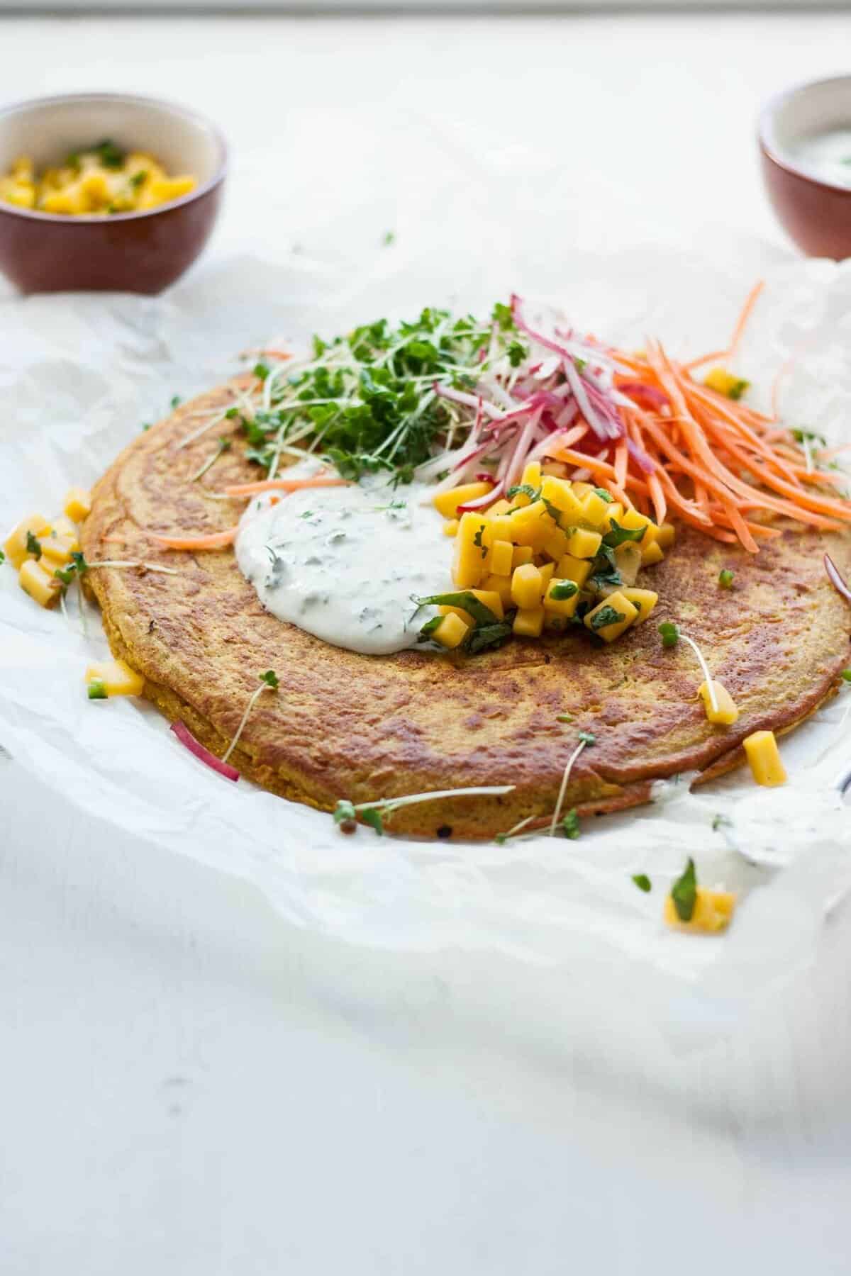 A onion bhaji pancake with mango salad and salad toppings on top.