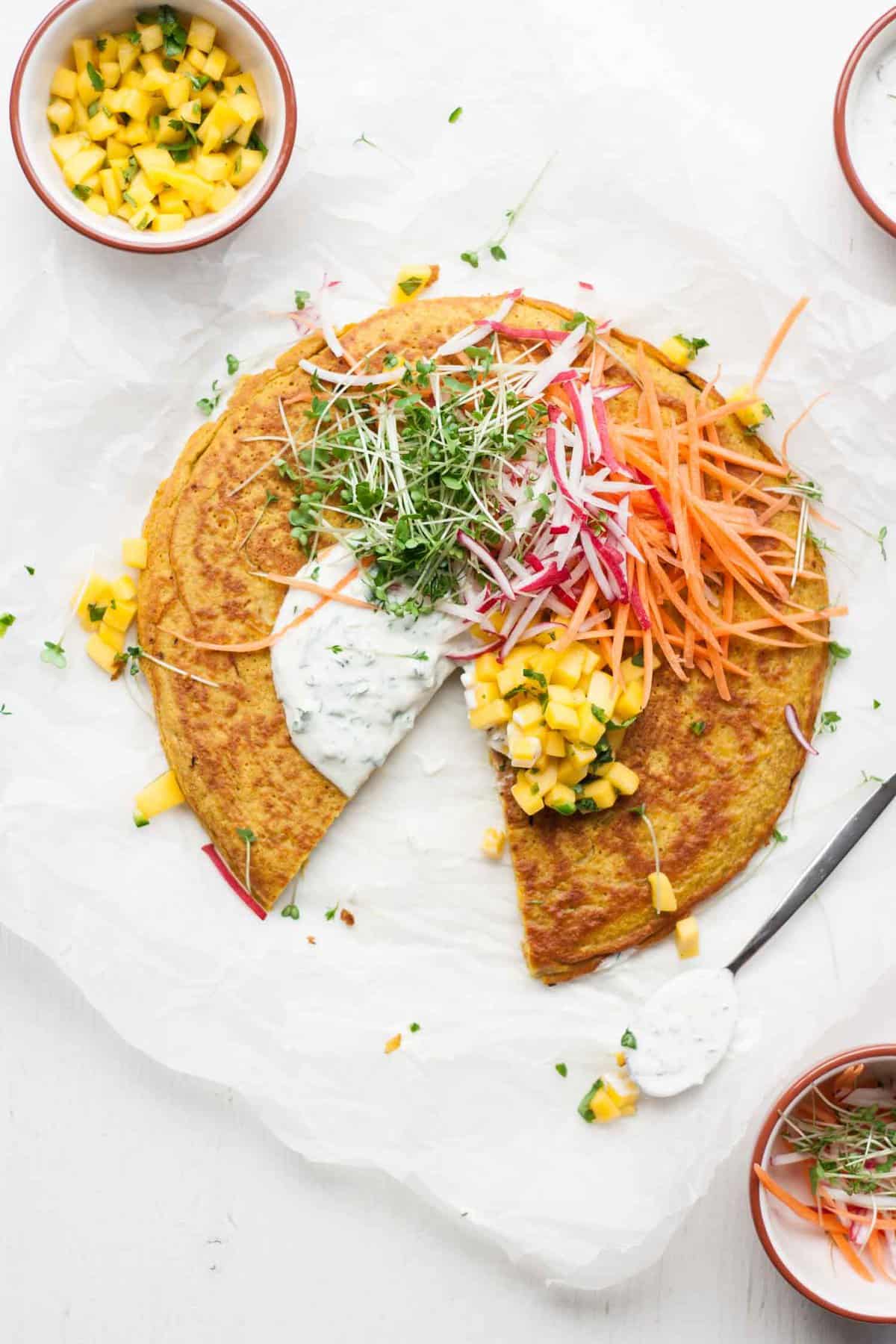 Onion bhaji pancake with salad toppings and a wedge cut out.