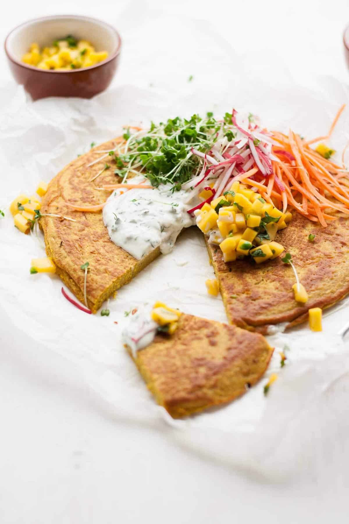 Close up of onion bhaji pancake with a slice cut and salad and salsa toppings.