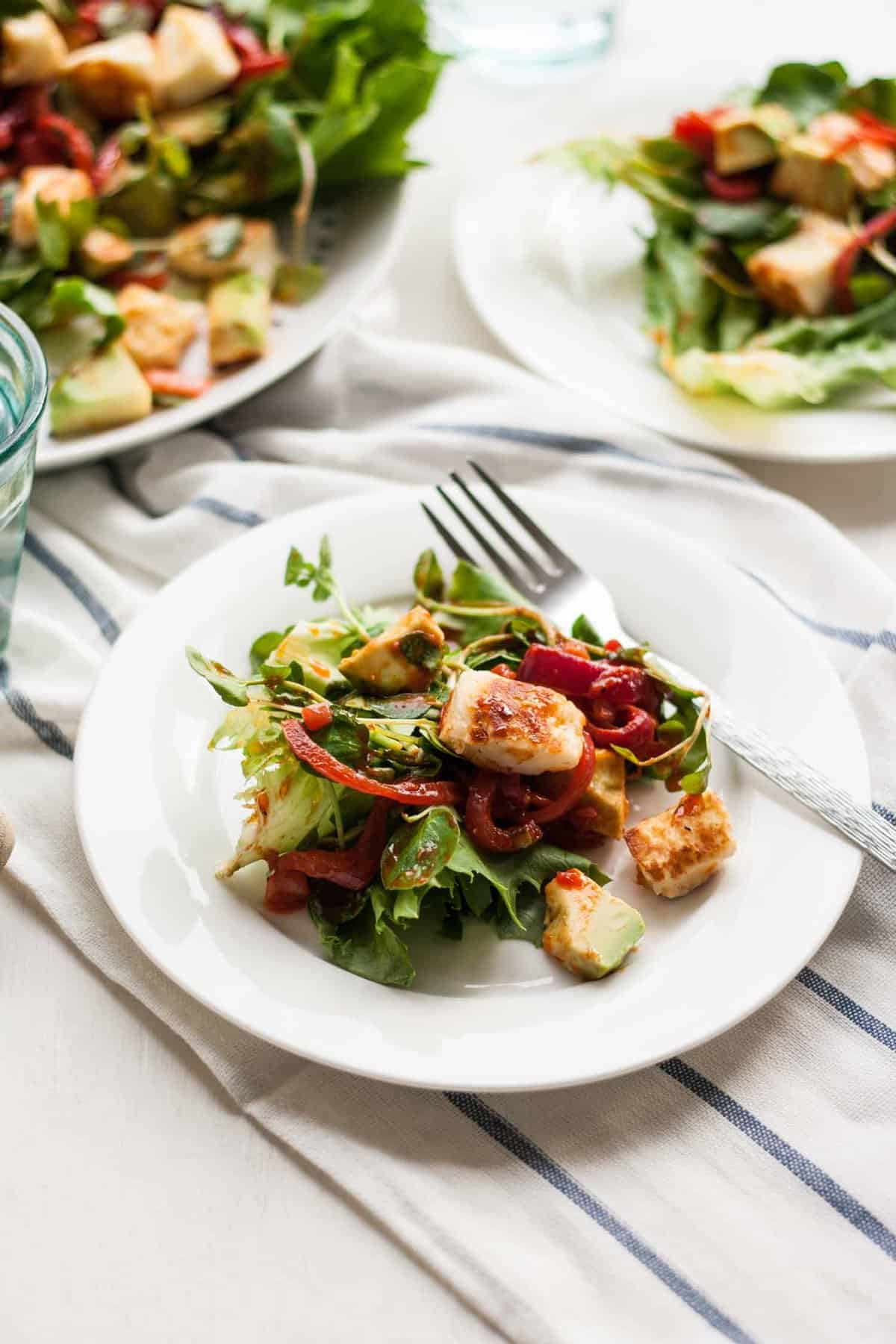 three plates with halloumi salad on with a fork.