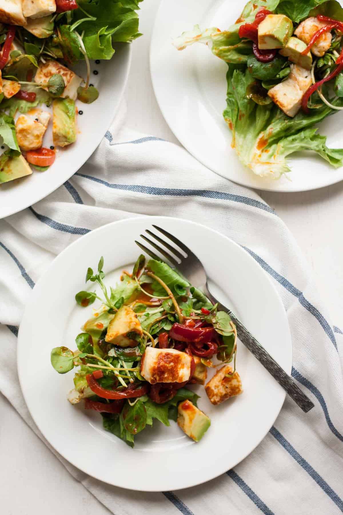 Three plates of halloumi salad with a fork on a napkin.