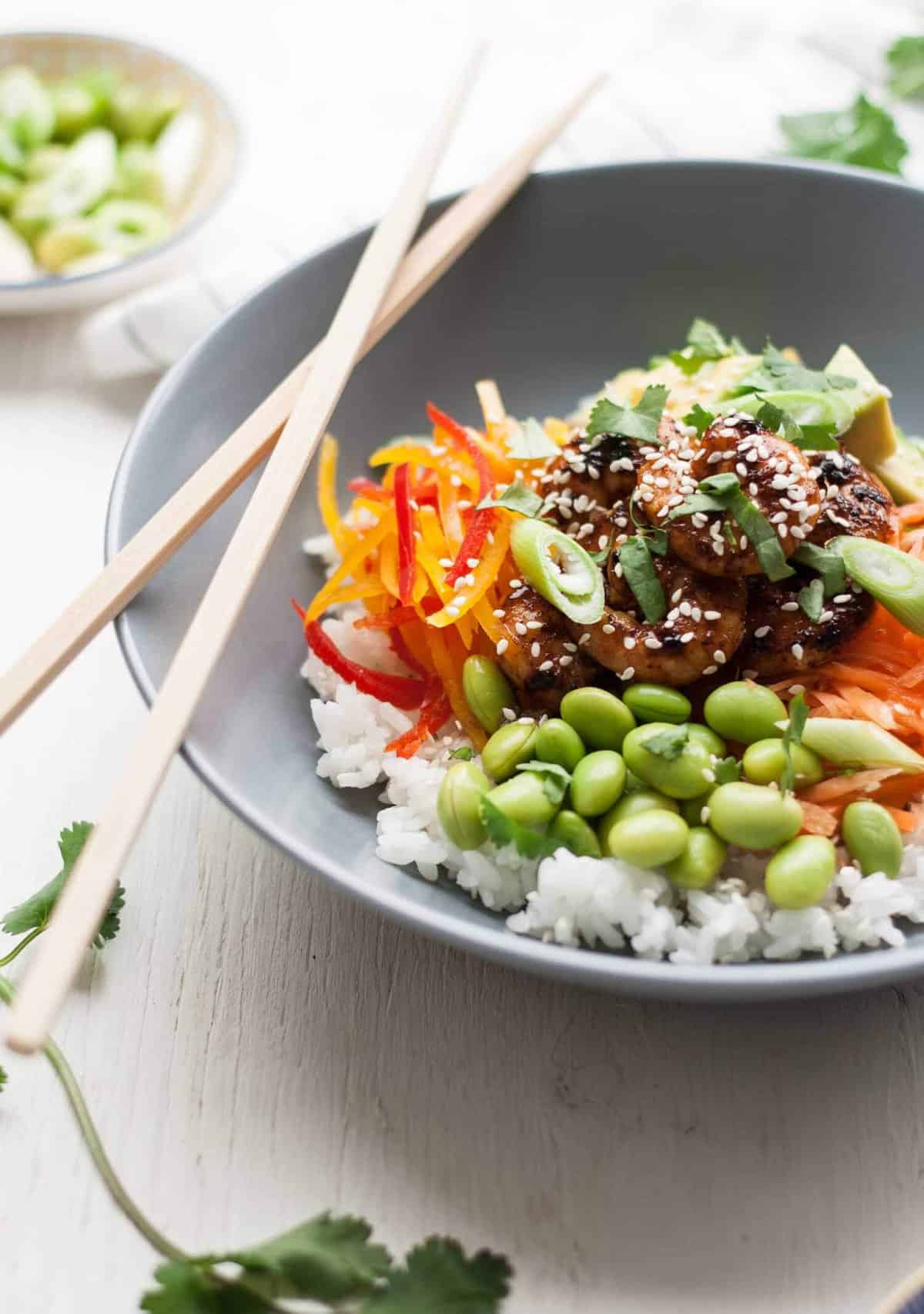 Prawns on veggies and rice in a bowl with chopsticks.