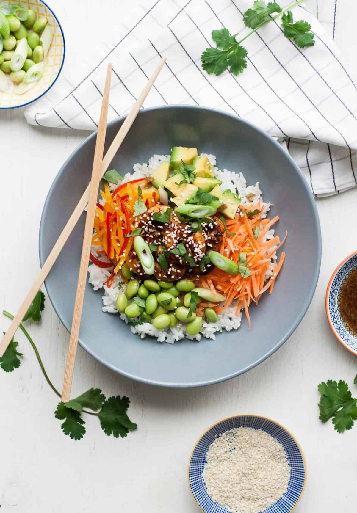 A plate of prawns, veggies and rice with chopsticks and napkin nearby.