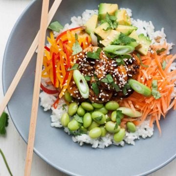 Spicy sticky prawns served with salad items on top of rice in a bowl with chopsticks.