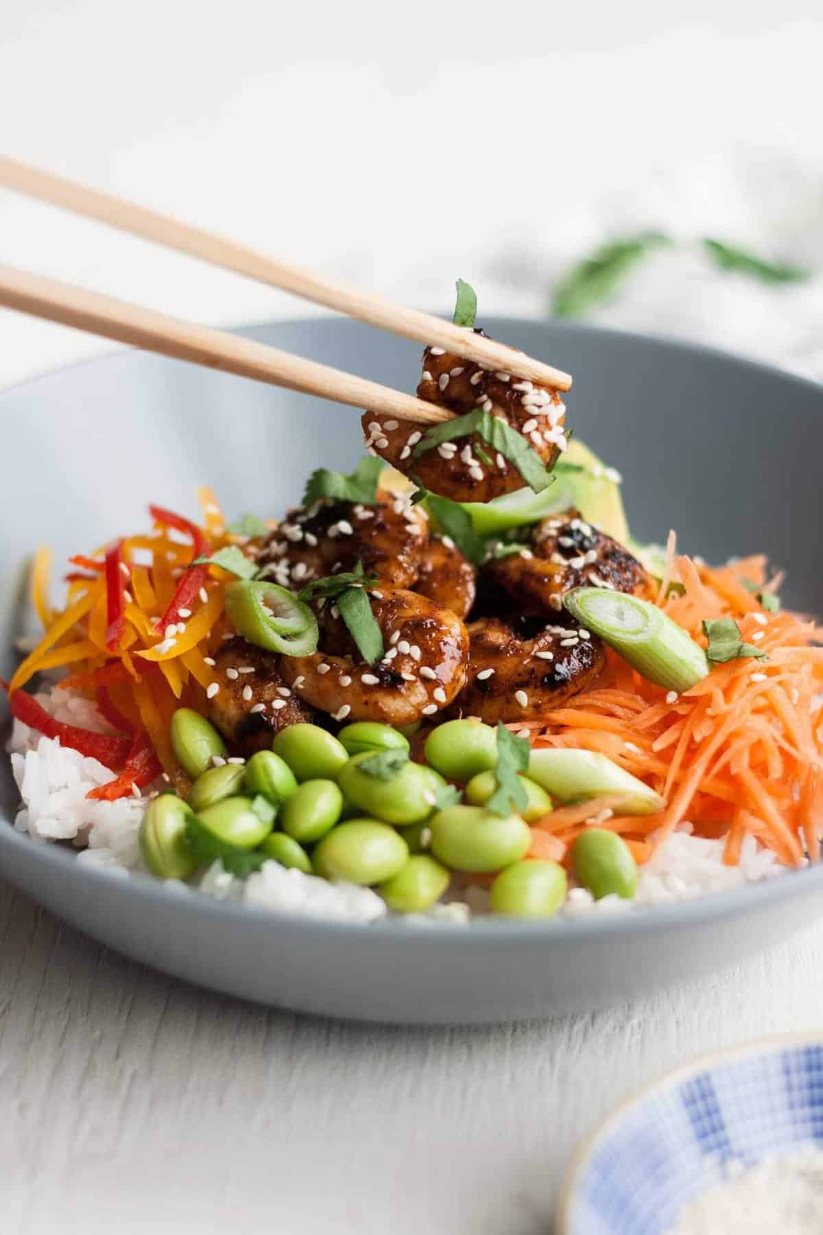 A prawn being held with chopsticks over a bowl.