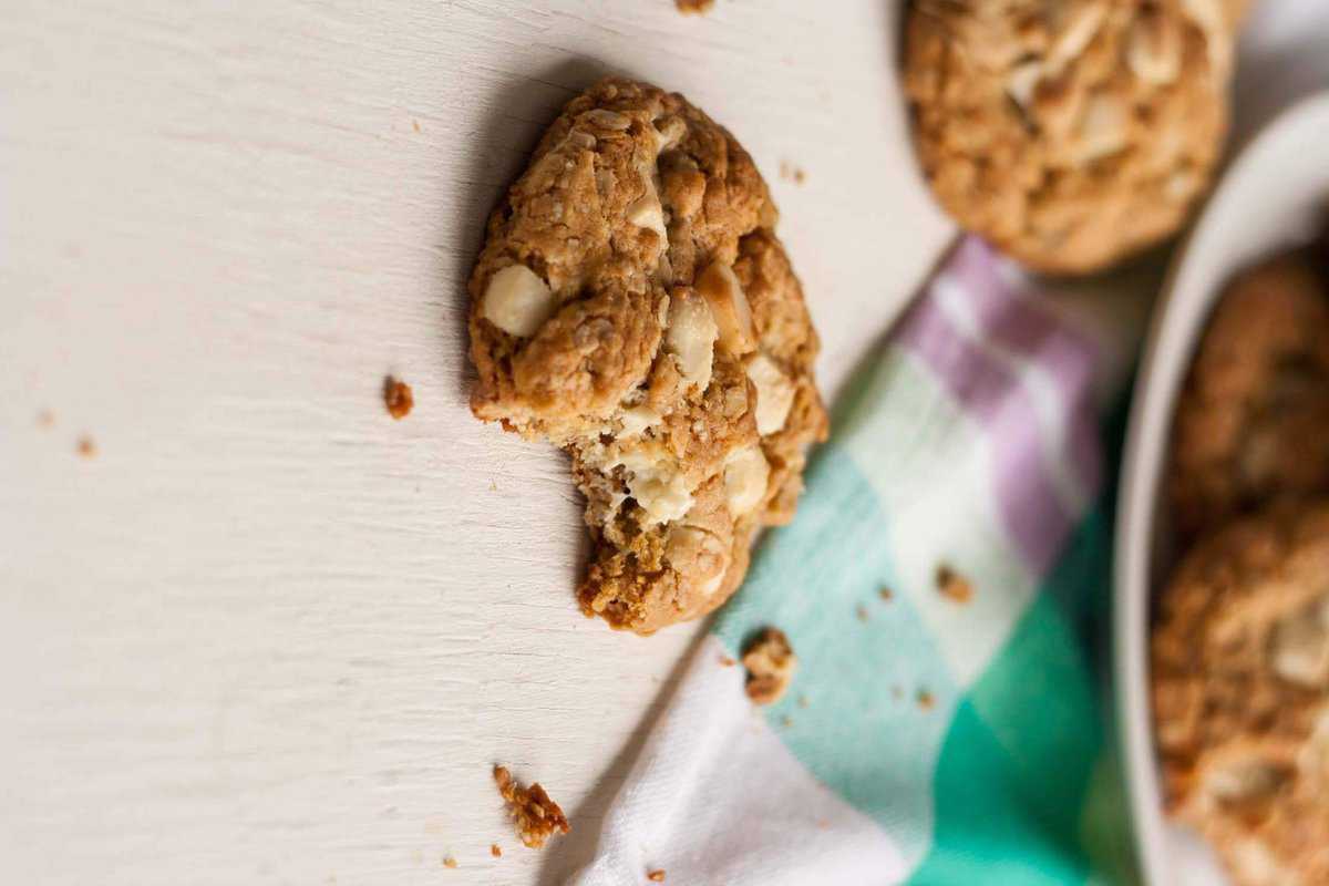 A close up of a white chocolate oatmeal cookie with a bite taken.