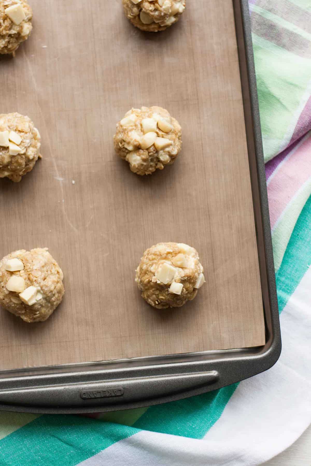 Multiple raw cookie dough balls with white chocolate chips and macadamia nuts.