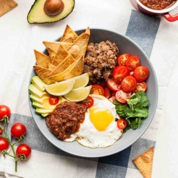 A bowl with refried beans tortillas, salsa, fried egg and salad.