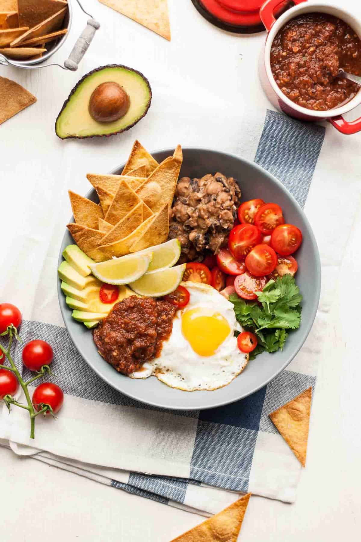 A bowl with refried beans tortillas, salsa, fried egg and salad.