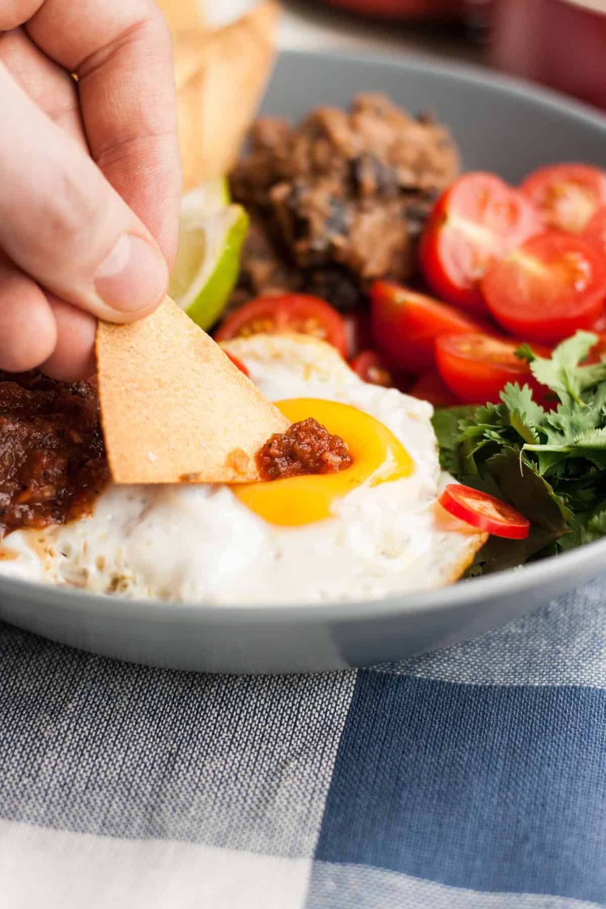 A close up of a person holding a tortilla chip dipping into an egg yolk.