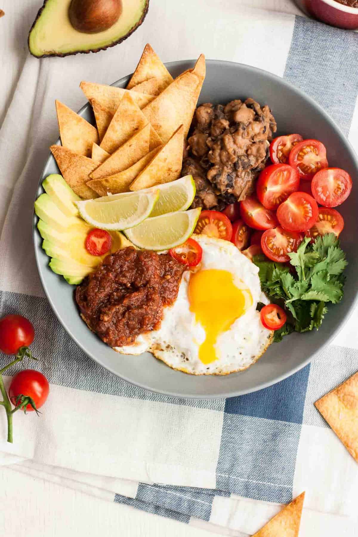 A bowl of salad items with a fried egg with a runny yolk.