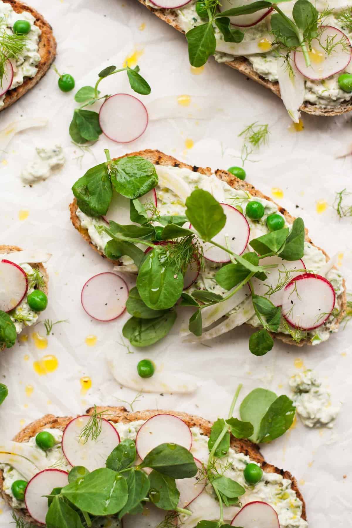 Close up of crostini topped with cream cheese radish and peashoots.