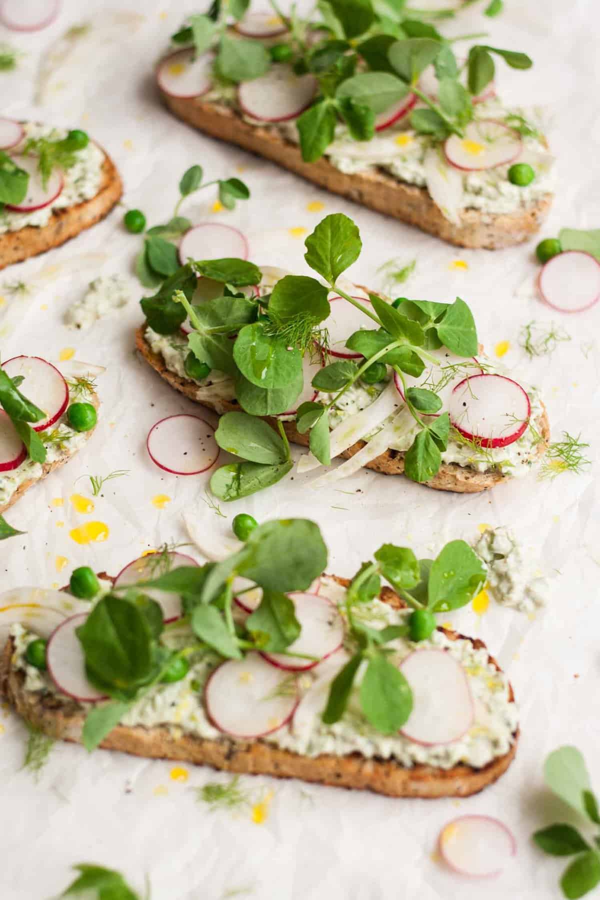 A slice of toasted bread topped with cream cheese, fennel, radish and peashoots.
