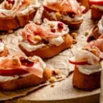 Ricotta crostini on a board with toppings and pomegranate arils to the side.