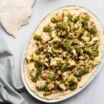 A plate with hummus topped with roasted cauliflower and chimichurri.