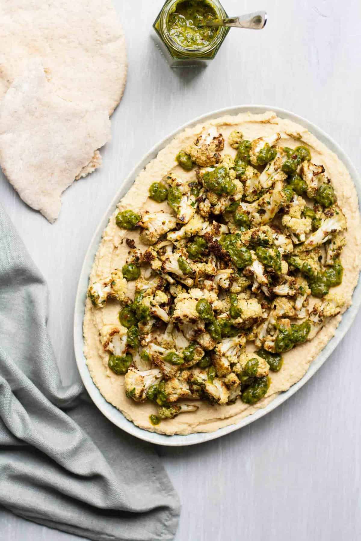 A plate with hummus topped with roasted cauliflower and chimichurri.