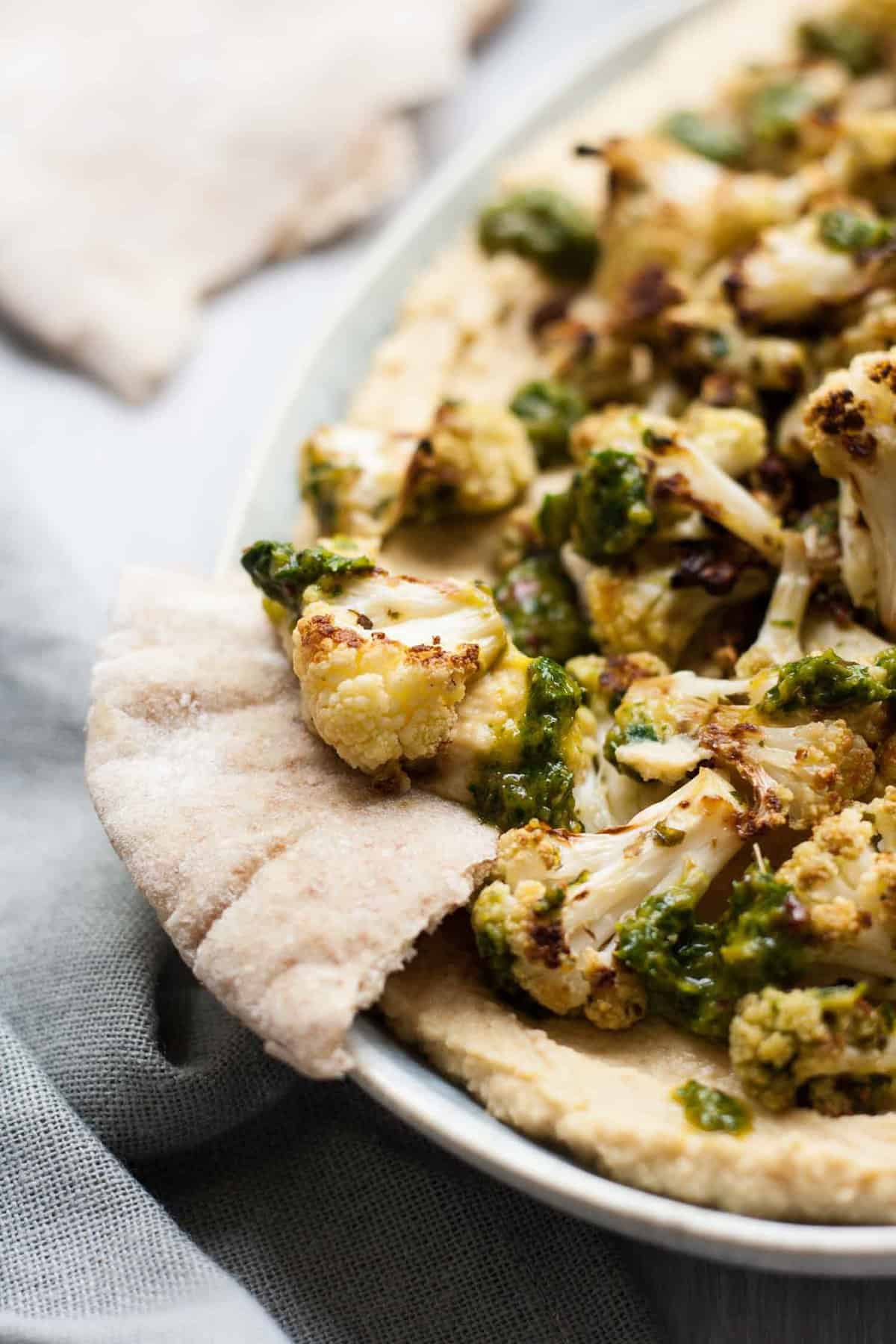 A pita scooping hummus and cauliflower on a plate.