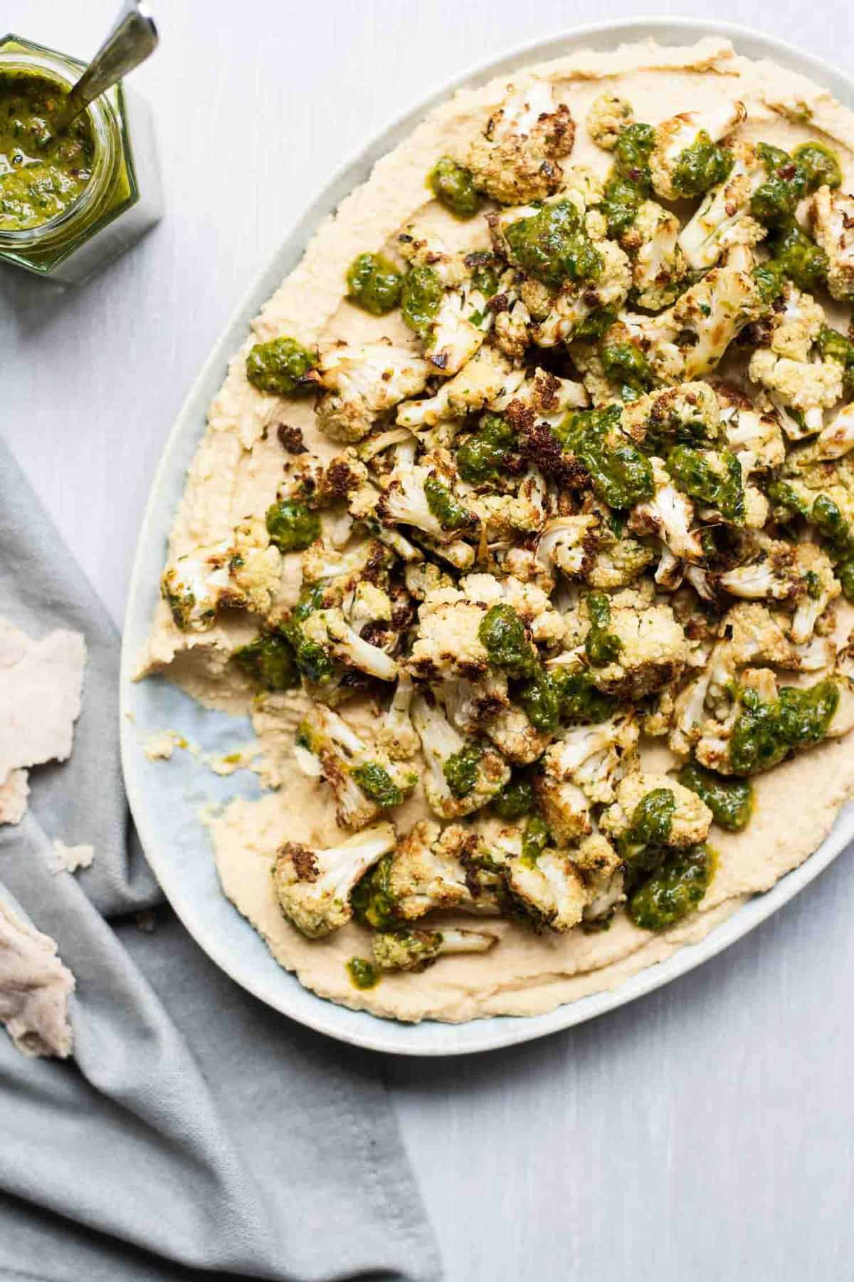 A pizza sitting on top of a plate of food, with Chimichurri and Cauliflower.