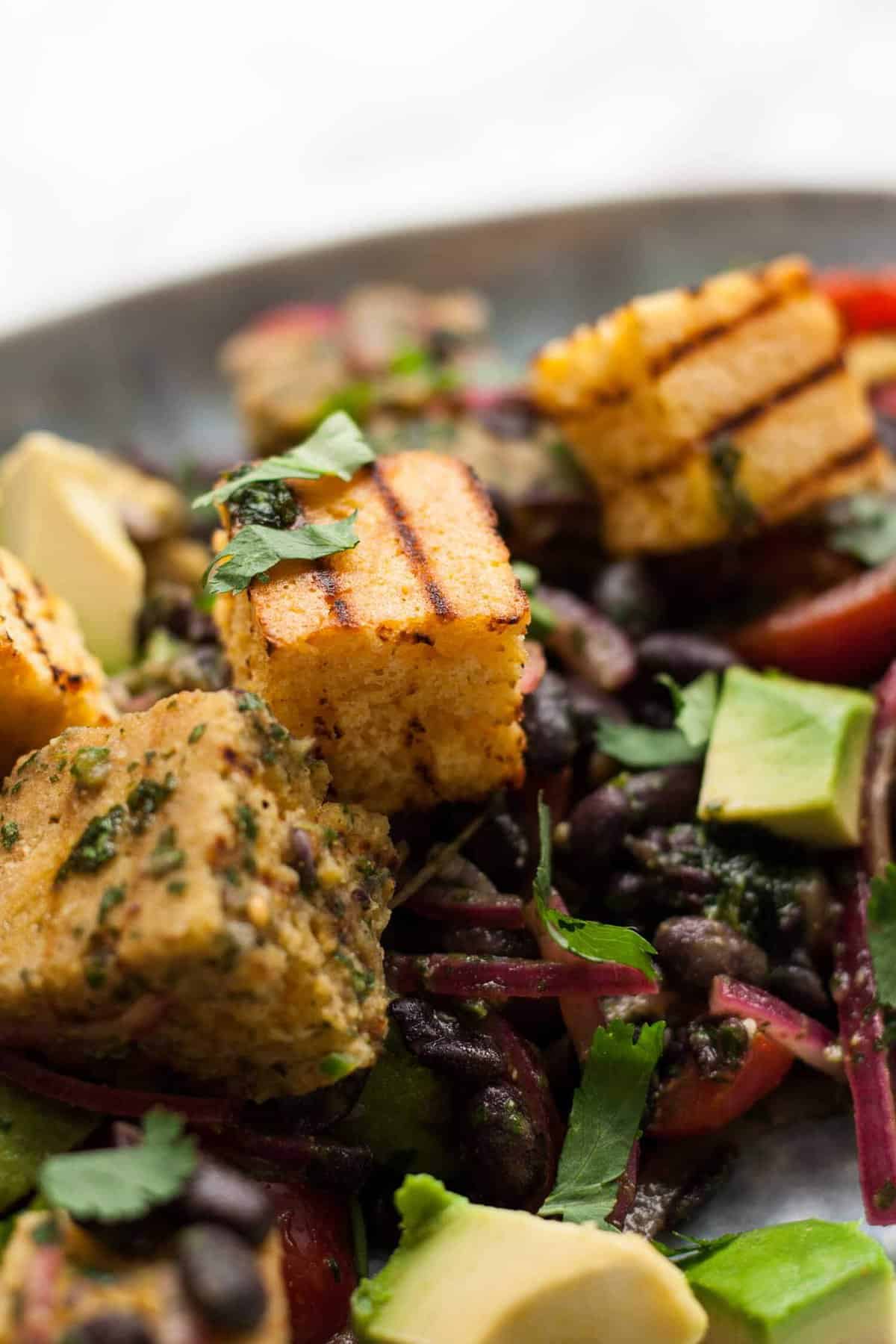 A close up of grilled corn bread salad on a plate with beans and avocado.