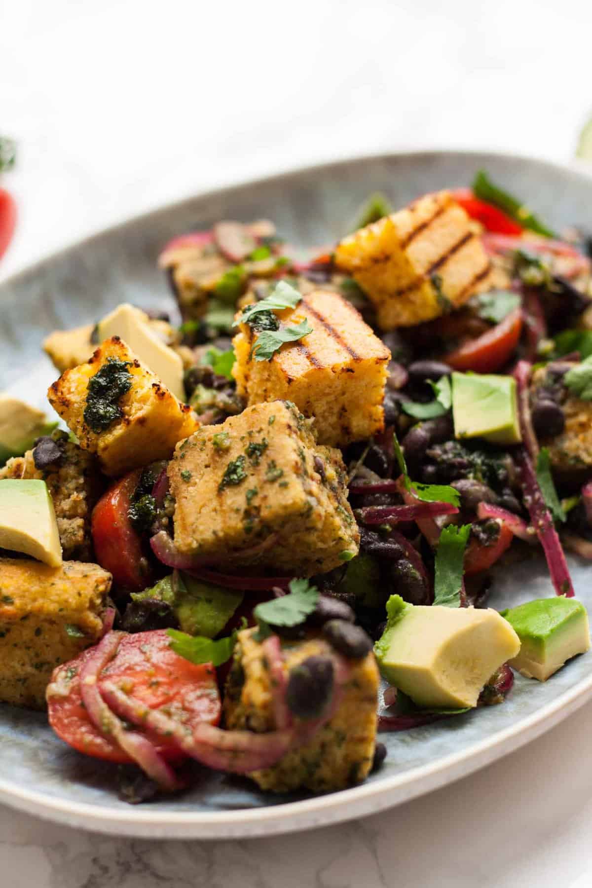 A plate of cornbread salad with avocado, tomatoes and beans.