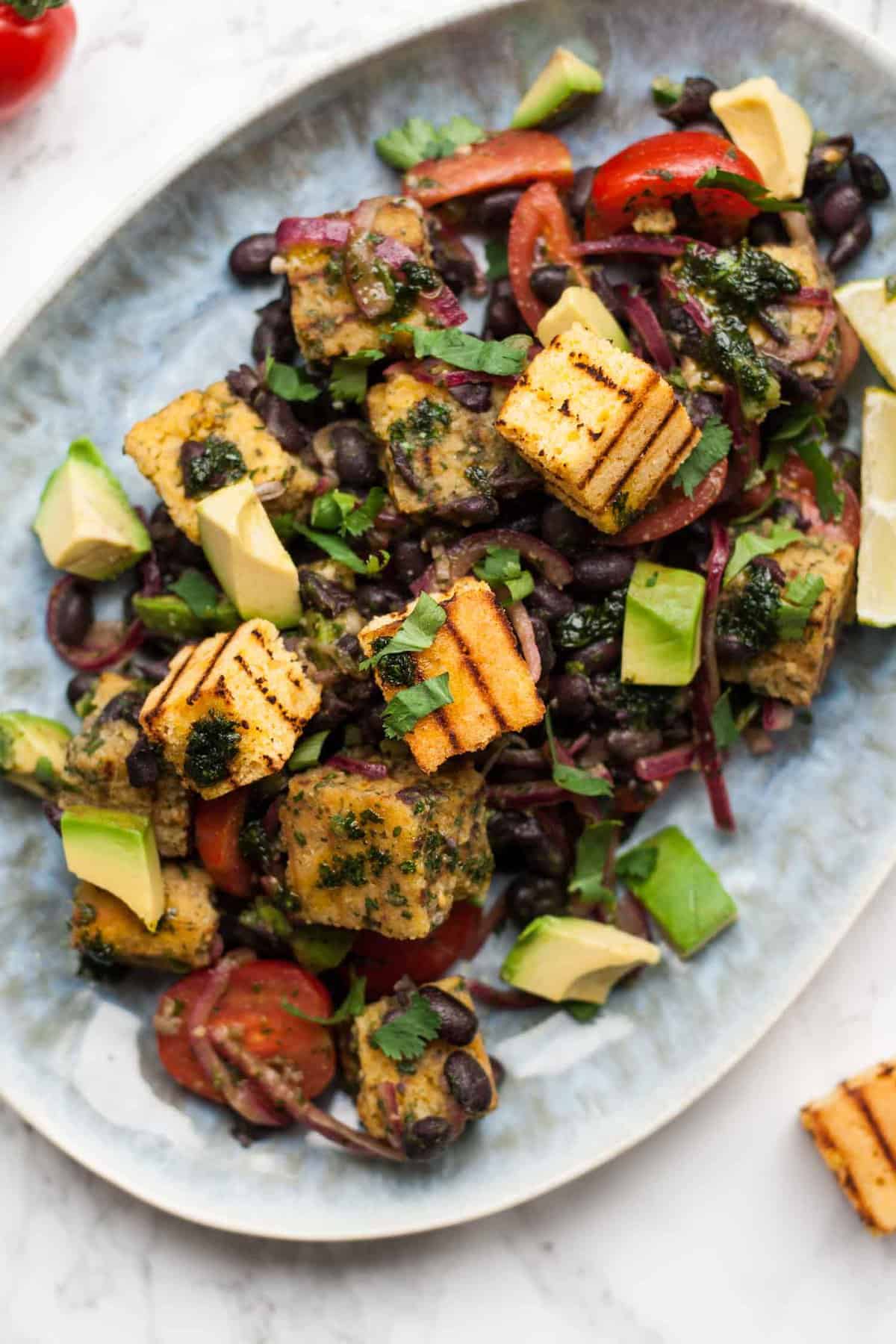 Close up of grilled cornbread bean salad on a plate with avocado on top.