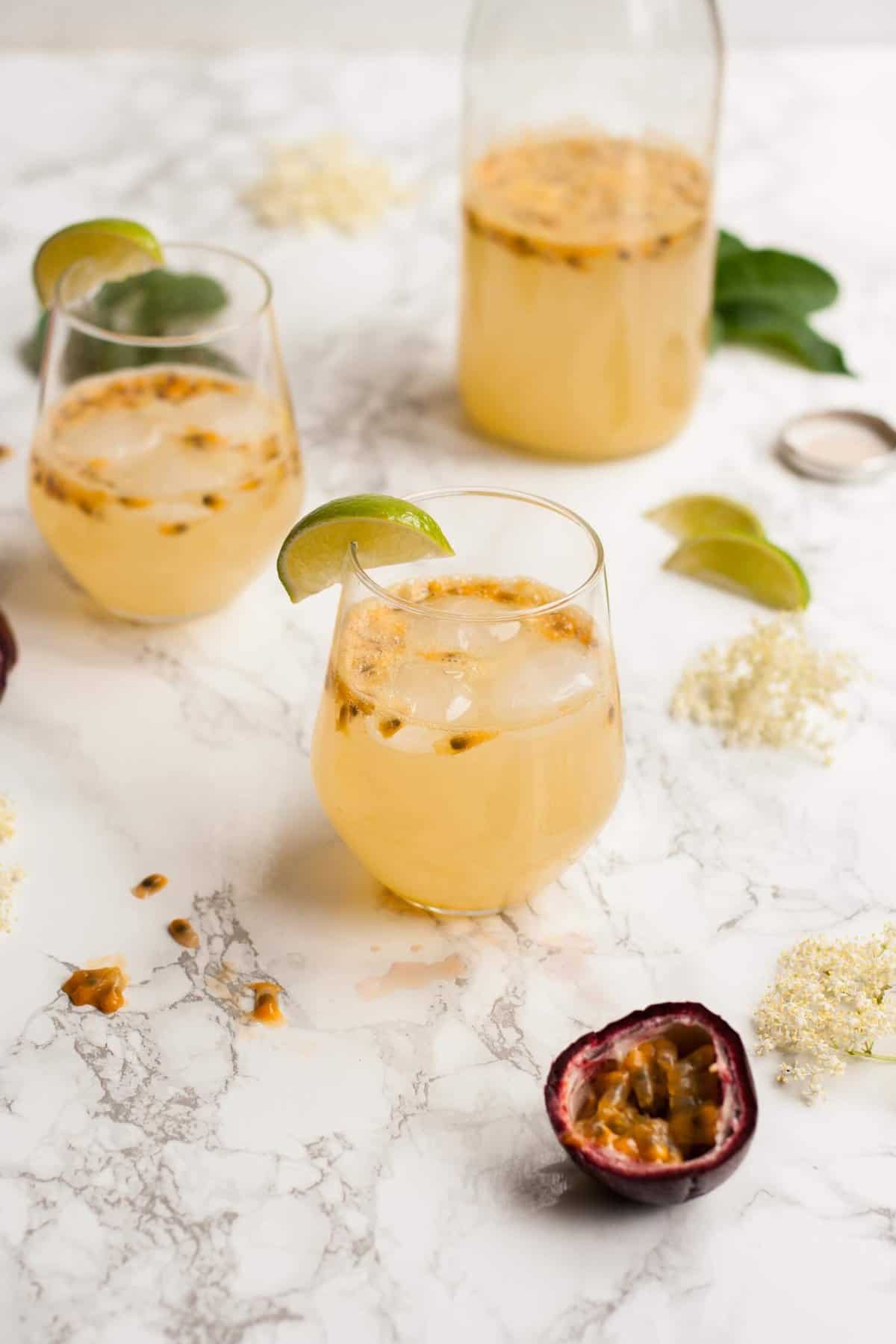 Multiple glasses of passionfruit mocktail with lime wedges on the edge on a marble surface.