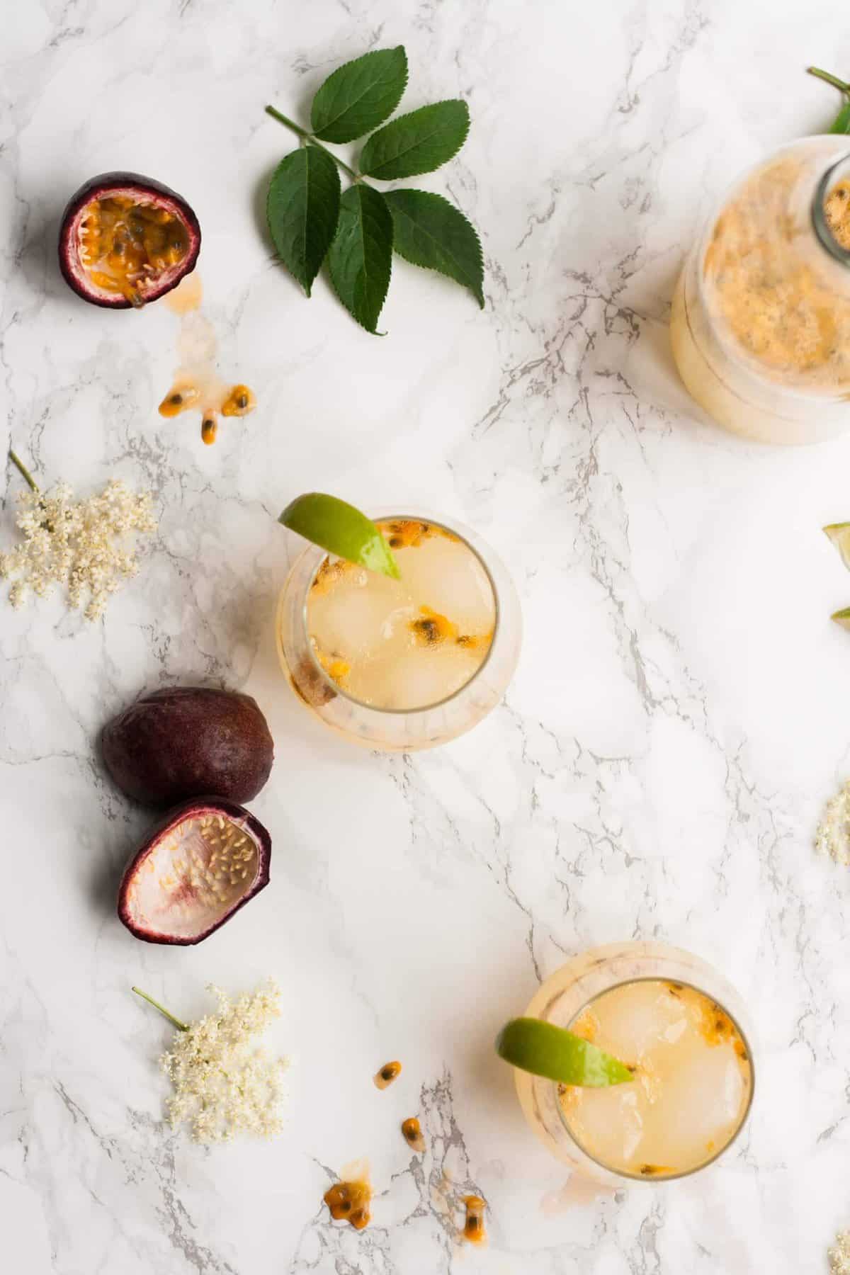 A glass of passionfruit mocktail with a lime wedge on the edge on a marble background.