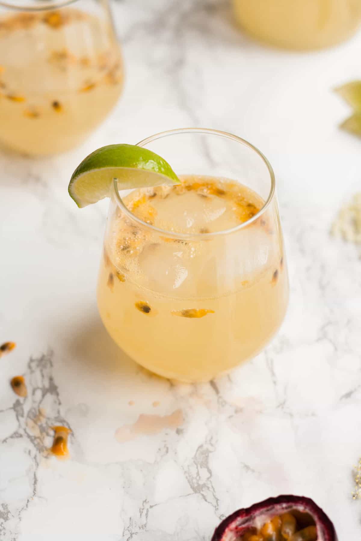 close up of a glass of passionfruit mocktail with a lime wedge on a marble surface.