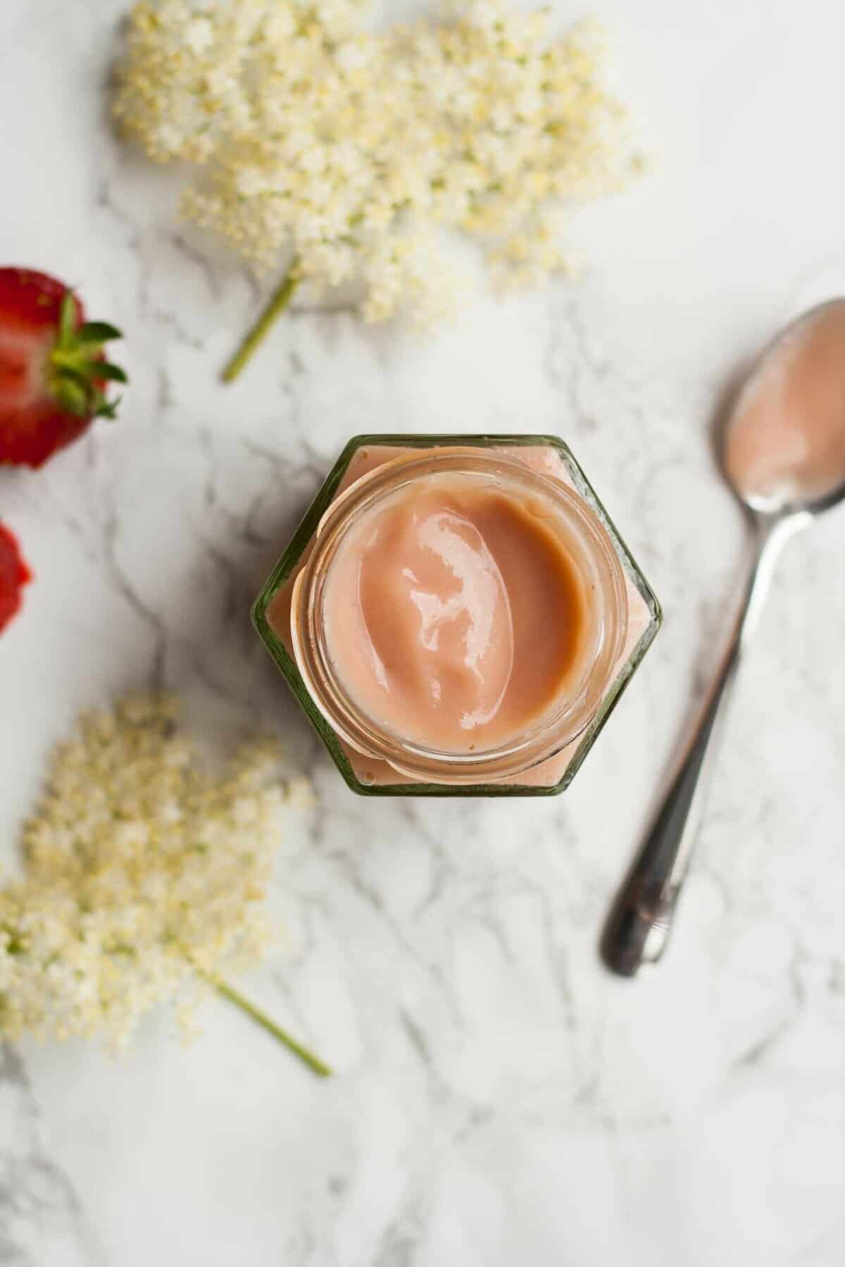 A jar of strawberry elderflower curd with a spoon to the side.