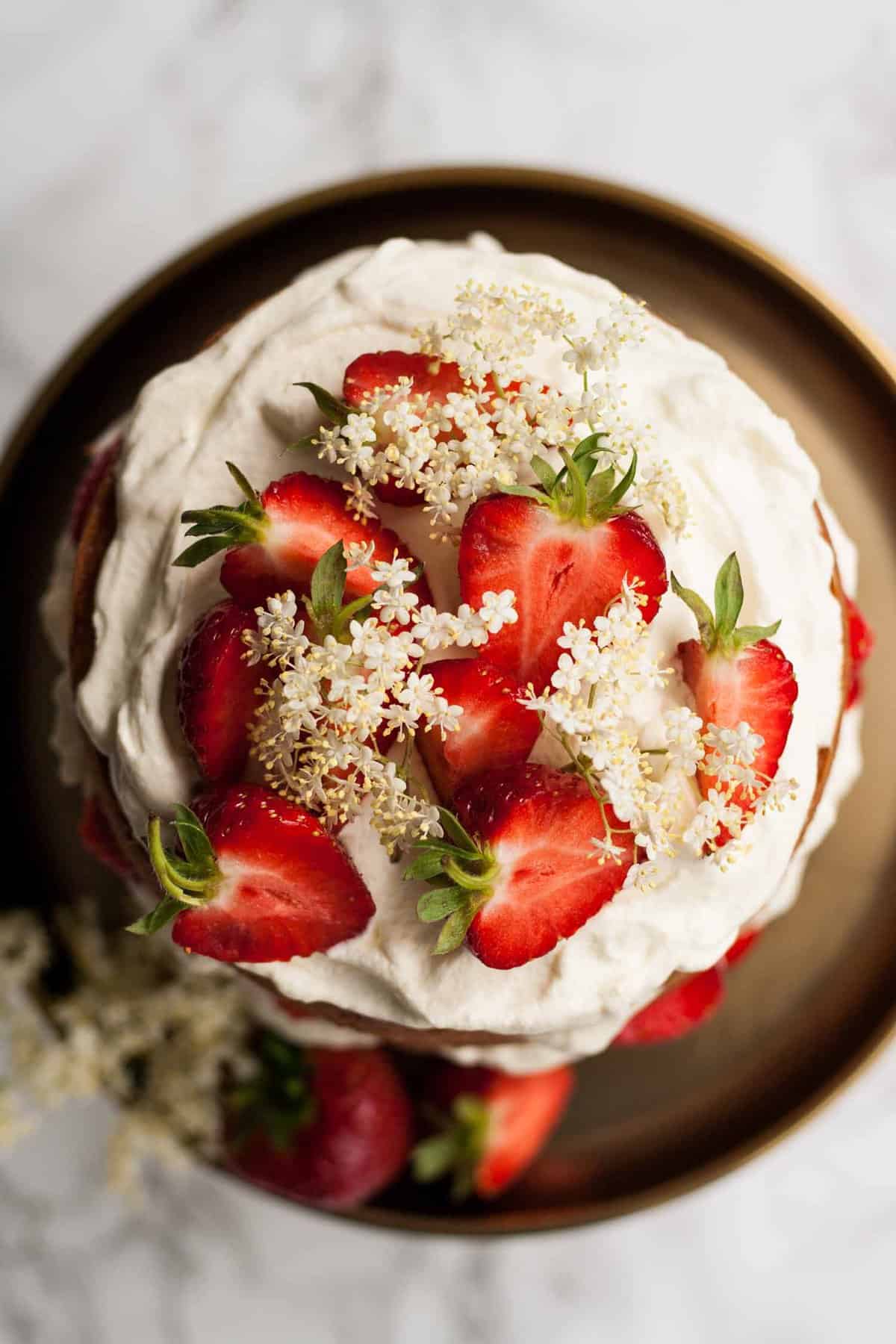 Close up of cream strawberries and elderflower on top of a cake.
