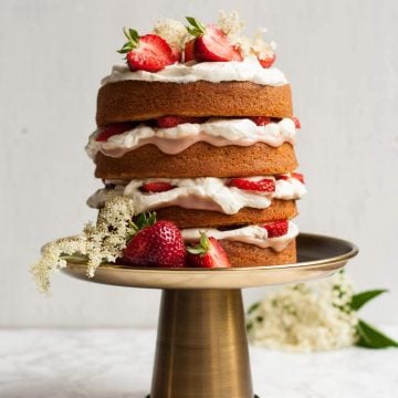 A triple layer sponge cake with cream and strawberry curd on a cake stand.