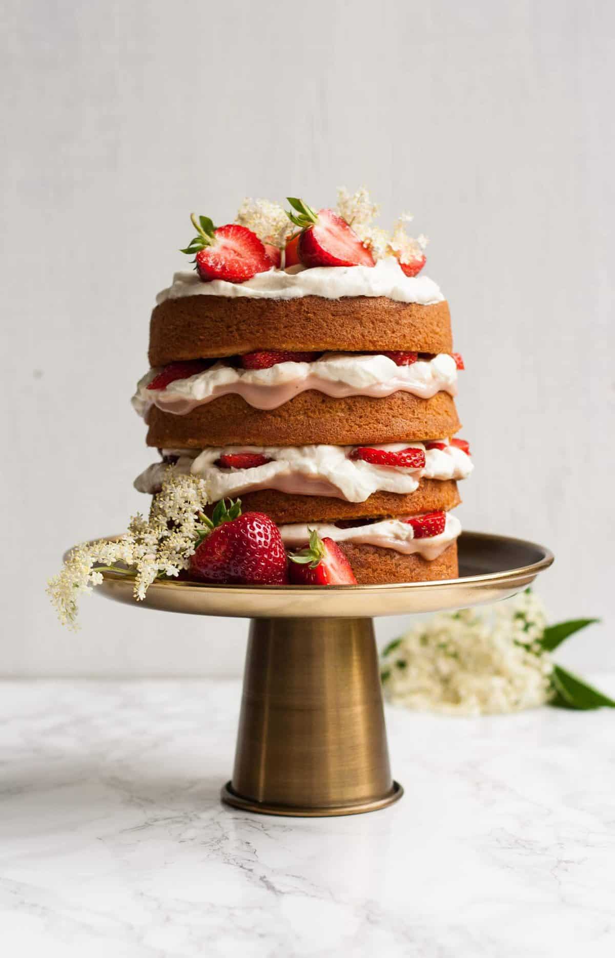 A triple layer sponge cake with cream and strawberry curd on a cake stand.