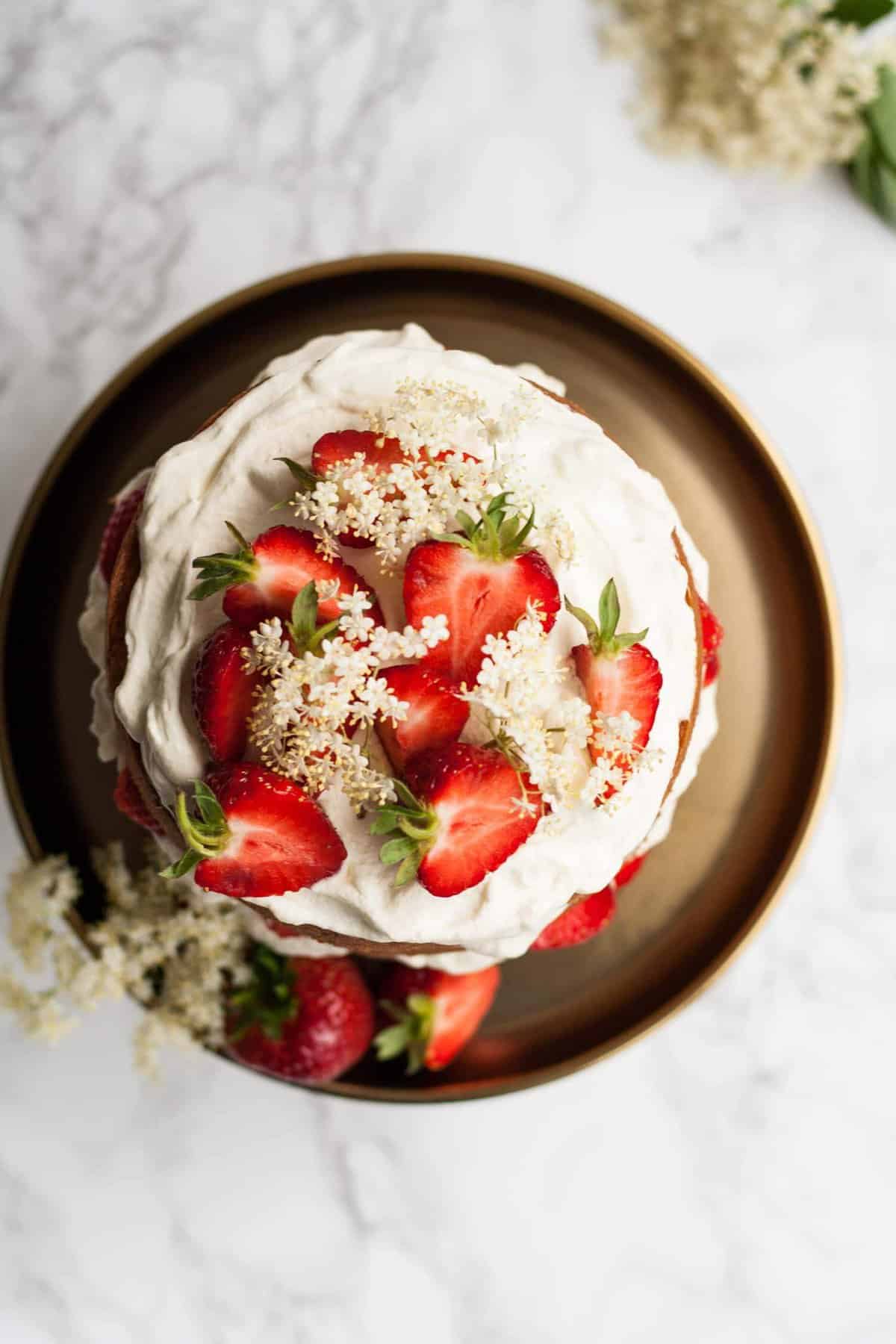 overhead of the top of cake topped with cream, strawberries and elderflowers.