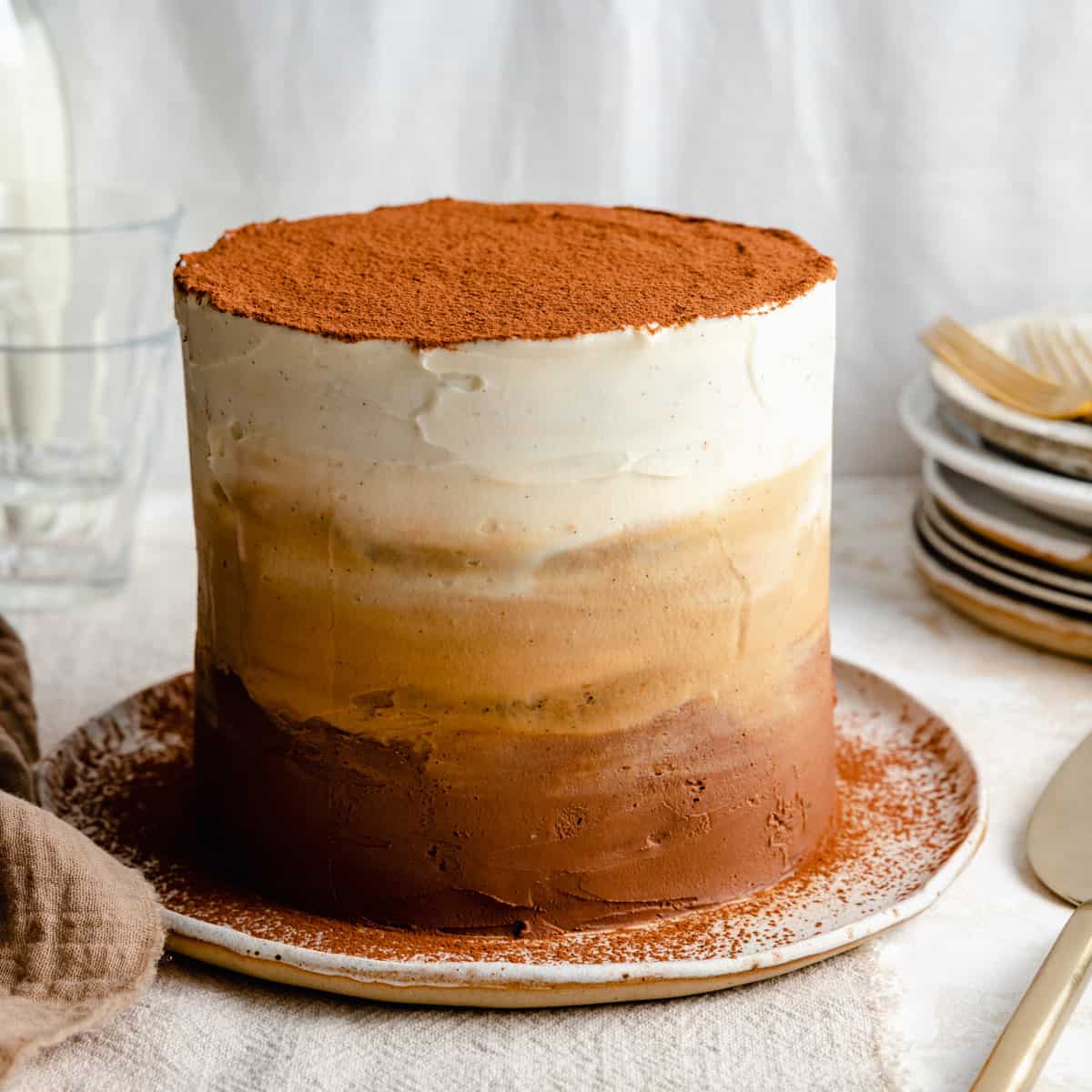 Tiramisu cake with ombre mascarpone frosting on a plate topped with a dusting of cocoa powder.