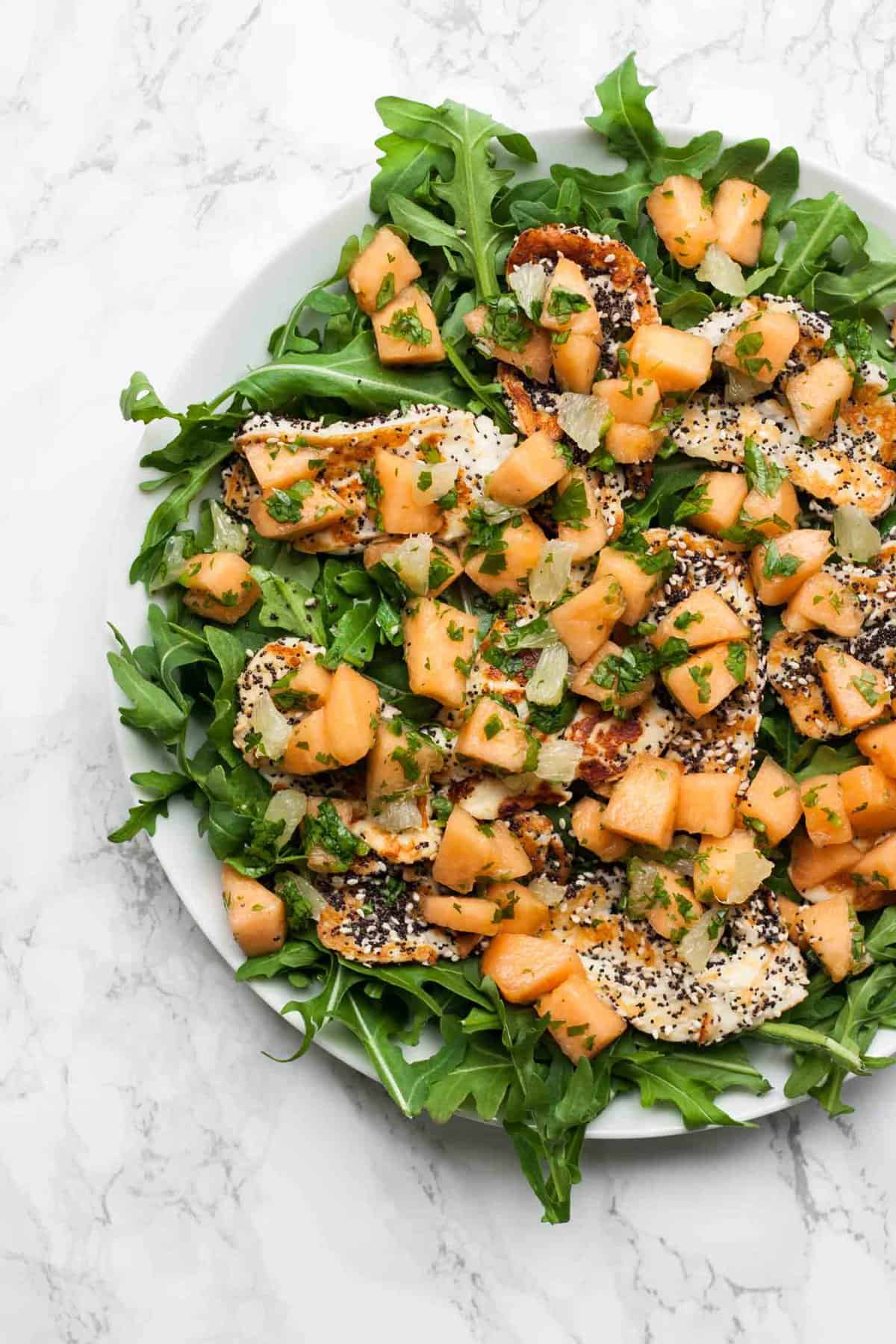 A platter with sesame crusted halloumi on top of salad leaves with marinated melon.