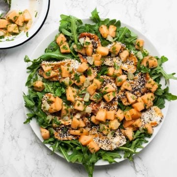 A platter with melon scattered on top of a halloumi salad.